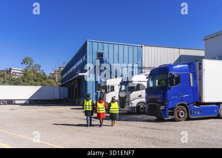 Logistikmitarbeiter in gut sichtbaren Westen, die an den Laderampen eines großen Industrielagers vorbeilaufen, als Kühler Stockfoto