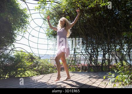 Junge Frau tanzt frei in grüner Pergola Stockfoto