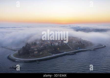 Eine Insel, umgeben von Nebel bei Sonnenaufgang mit ruhigem Wasser. Aus der Vogelperspektive auf dicken Nebel fällt über die Nessebar, Burgas, Bulgarien Stockfoto
