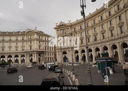 Große symmetrische Gebäude, die die Piazza della Repubblica in Rom umrahmen, zeigen den Verkehr, geparkte Autos und einen traditionellen Kiosk auf dem breiten, gepflasterten Platz Stockfoto