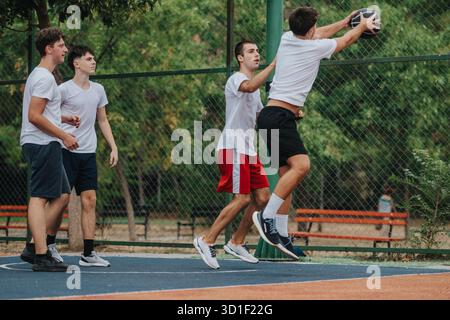 Junge Männer spielen Basketball auf einem Platz im Freien, Sprungmoment, Teamarbeit und Freundschaft. Stockfoto