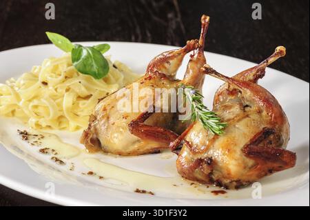 Gebratene oder gebratene Wachteln mit Kräutern und Tagliatelle auf weißem Teller auf Holztisch Stockfoto