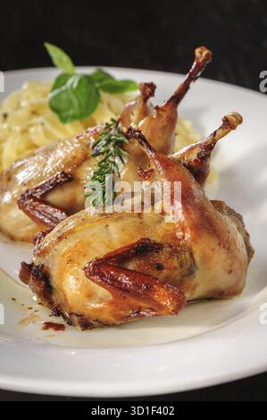 Gebratene oder gebratene Wachteln mit Kräutern und Tagliatelle auf weißem Teller auf Holztisch Stockfoto