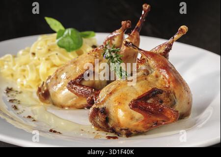 Gebratene oder gebratene Wachteln mit Kräutern und Tagliatelle auf weißem Teller auf Holztisch Stockfoto