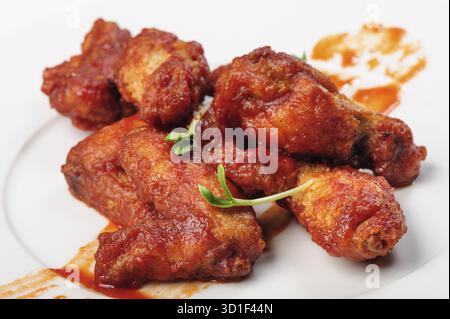 Gebratene Hähnchenschenkel in roter, scharfer Karamellsauce mit grünen Bohnensprossen auf weißem Teller Stockfoto