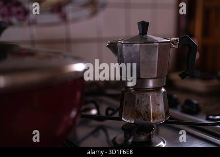 Moka-Topf, der reichhaltigen, dampfenden Kaffee auf einem Gasherd in einer gemütlichen Hausküche aufbrühen lässt, erinnert an traditionelles italienisches Morgenritual, rustikales Metall, Aroma und W Stockfoto