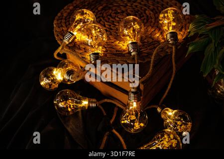 Nahaufnahme leuchtender dekorativer Lichterketten mit kleinen getrockneten Blumen, die in einer Holzkiste in einer gemütlichen dunklen Umgebung platziert werden. Stockfoto