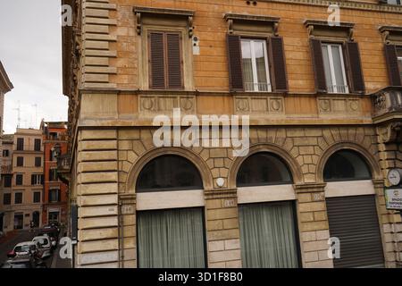 Klassische römische Gebäudefassade mit warmen Ocker- und Terrakottafönen, bogenförmigen Schaufensterfenstern und typischen Fensterläden. Stockfoto