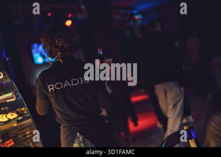 Este, italien 28. oktober 2025: Die Kellnerin stürmt sich durch einen lebhaften, dunklen Nachtclub mit einem Tablett voller Drinks in unscharfer Bewegung, Lichtern und hektischer Nacht Stockfoto