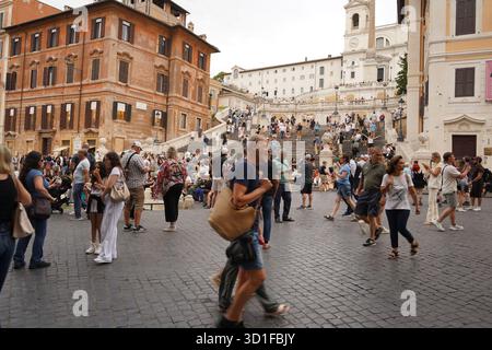 Ein belebter Platz am Fuße der Spanischen Treppe in Rom, wo an einem Sommertag eine Menge Touristen über das Kopfsteinpflaster spazieren. Stockfoto