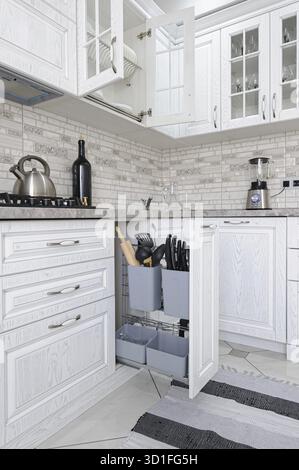 Innenraum der modernen weißen Holzküche in einem luxuriösen Haus, einige Schubladen sind offen Stockfoto