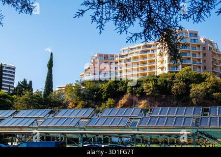 Sonnenkollektoren und moderne Wohngebäude an einem sonnigen Tag. Solarpaneele unter Wohngebäuden auf einem grünen Hügel. Konzept der erneuerbaren Energien Stockfoto