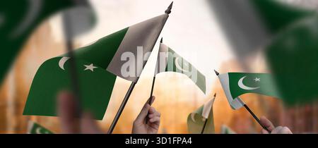 Pakistanische Flaggen in den Händen vor einem verschwommenen urbanen Hintergrund. Die Fotoillustration wurde ohne künstliche Intelligenz erstellt, nur mit Photoshop. Stockfoto