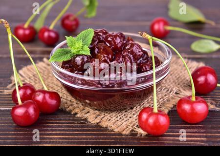 Kirschmarmelade in einer Glasschale und frische Kirschen auf hölzernem Hintergrund. Nahaufnahme. Stockfoto