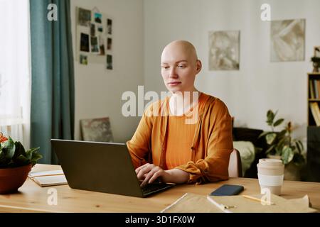Porträt einer jungen erwachsenen Frau mit Alopezie mit Laptop am Schreibtisch Stockfoto