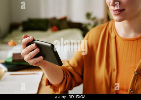 Junge Erwachsene Frau Lächelt, Während Sie Ihr Smartphone Drinnen Hält Stockfoto