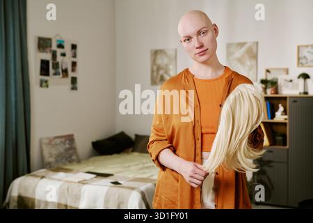 Porträt einer jungen erwachsenen Frau, die blonde Perücke hält und sanft lächelt Stockfoto