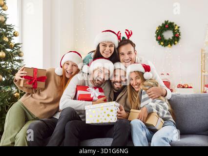 Glückliche junge Freunde sitzen auf dem Sofa, umarmen, Geschenke austauschen und gemeinsam Weihnachten feiern. Stockfoto