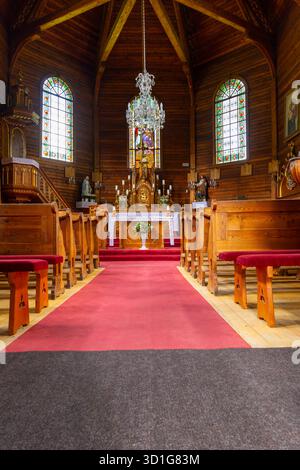 Innenraum einer traditionellen Holzkirche mit Altar, Bänken, Buntglas und rotem Teppich Stockfoto