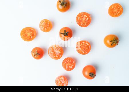Flache Lage frischer Kirschtomaten, ganz und in Scheiben geschnitten, verstreut auf einem sauberen weißen Hintergrund. Minimalistisches Essensmuster mit viel Kopierraum. Stockfoto