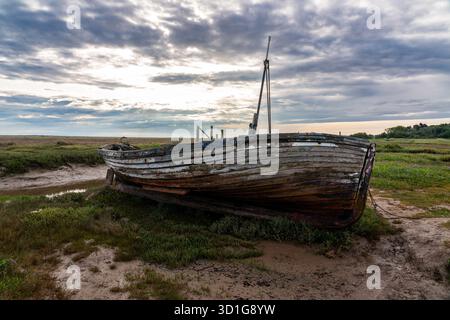 Verlassenes Holzboot, das auf Wattflächen unter bewölktem Himmel ruht Stockfoto