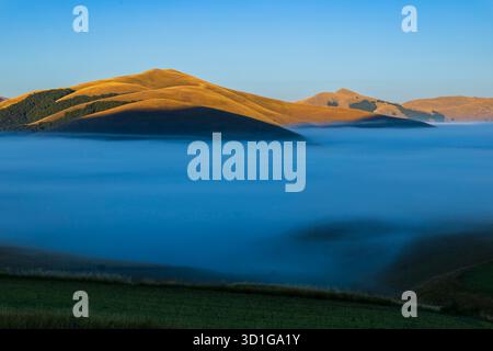 Berge, die sich über einen niedrigen Nebel erheben und bei Sonnenaufgang ein Tal füllen Stockfoto