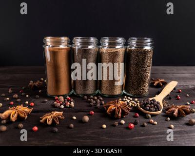 Eine künstlerische Anordnung verschiedener Gewürze in Glasgläsern auf einer rustikalen Holzoberfläche mit Zimtstangen und einer Auswahl an farbenfrohen Pfeffermörsern Stockfoto