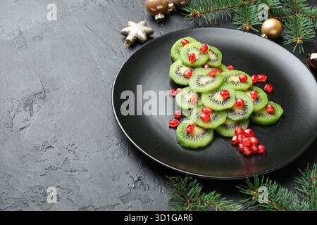 Weihnachtsbaum aus Kiwi, Granatapfelkernen und festlicher Dekoration auf schwarzem Tisch, Nahaufnahme. Leerzeichen für Text Stockfoto
