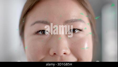 Zeigt eine koreanische Frau in Nahaufnahme, die das Gesicht in einem sanft beleuchteten Innenraum mit grünen dreieckigen Fragmenten scannt Stockfoto