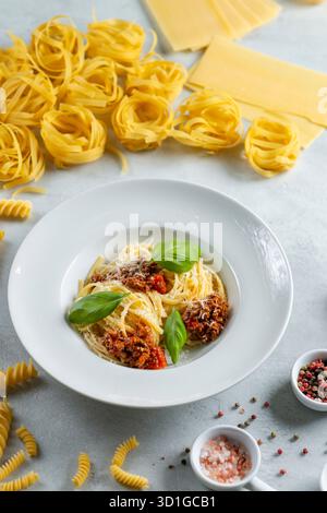 Spaghetti Bolognese auf einem Teller, umgeben von verschiedenen rohen Nudelsorten und Gewürzen Stockfoto