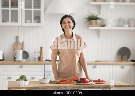 Küchenporträt glückliche Seniorin, die am Tisch steht und Salat hackt Stockfoto