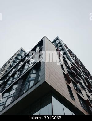 Blick auf die Fassade eines modernen Gebäudes mit großen Fenstern. Ecke eines stilvollen Bürogebäudes bei Regen und klarem bewölktem Himmel. Stockfoto