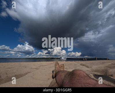 Ein ruhiger Blick auf den Strand mit sandigem Ufer und dramatischen Wolken, die sich über dem Himmel sammeln, perfekt für Entspannung oder Naturprojekte. Stockfoto