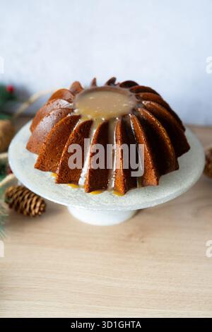 Saisonaler Bundt-Kuchen mit einer reichen Karamellglasur auf einem Kuchenständer mit Weihnachtsdekoration. Perfektes Dessert für Winterfeiern. Stockfoto