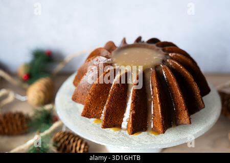 Saisonaler Bundt-Kuchen mit einer reichen Karamellglasur auf einem Kuchenständer mit Weihnachtsdekoration. Perfektes Dessert für Winterfeiern. Stockfoto