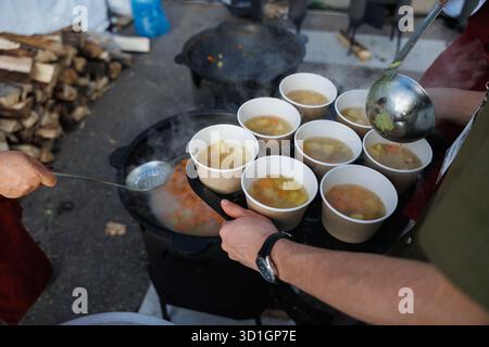 Engagierte Freiwillige servieren köstliche heiße Suppe in ökologisch biologisch abbaubaren Tassen, um die Bedürfnisse der Gemeinschaft zu unterstützen Stockfoto