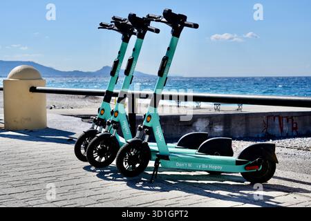 Eine Reihe von elektrischen Hoppy-Motorrollern mit blauem Meer dahinter. Stockfoto