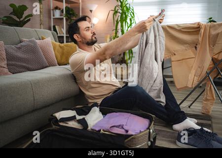 Mann, der Kleidung für eine Reise in sein Wohnzimmer packt Stockfoto