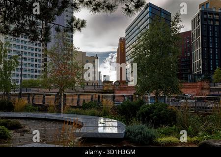 Die nassen Gedenksteine der Lichtglade leuchten, wenn die Sonne durch einen stürmischen Himmel mit Wolkenkratzern im Hintergrund bricht, Manchester, England. Stockfoto