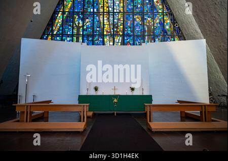 Die Arktische Kathedrale, Tromso, Norwegen. Ein heiterer Altar mit einem Buntglasfenster darüber, flankiert von Holzbänken, befindet sich in einem modernen Kircheninnenraum Stockfoto