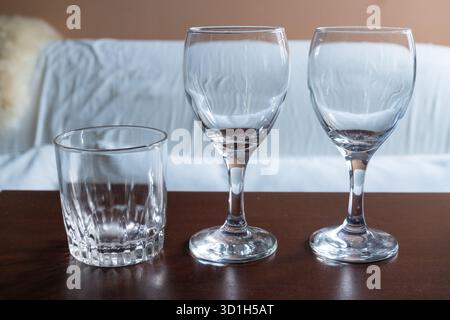 Drei leere Trinkgläser – ein kurzer, gemusterter Tumbler und zwei Stielweingläser – sind ordentlich auf einer dunklen, polierten Holzoberfläche Agave angeordnet Stockfoto