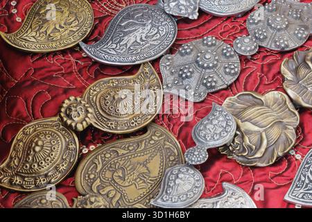 Eine Kollektion handgefertigter Metallverzierungen mit detaillierten Mustern und kulturellen Motiven, die auf sattem rotem Stickstoff angeordnet sind. Das Bild wird hervorgehoben Stockfoto