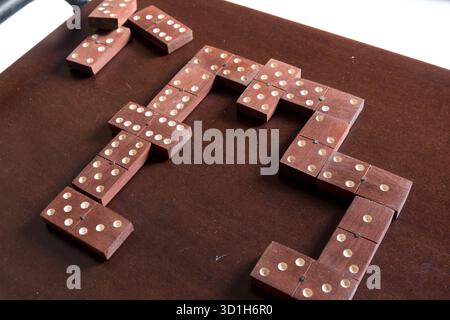 Ein klassisches Spiel alter hölzerner Dominosteine liegt auf einem dunklen Holztisch, bereit zum Spielen. Die Stücke sind ein sattes, dunkelbraunes mit weißen Punkten. Stockfoto