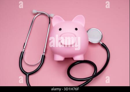 Eine pinkfarbene Schweinebank sitzt neben einem Stethoskop vor rosafarbenem Hintergrund. Stockfoto
