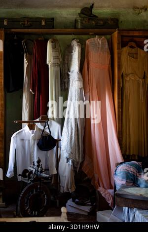 Vintage-Schlafzimmer-Inneneinrichtung mit antikem Wecker und Glasflaschen auf hölzernem Nachttisch neben ungebackenem Bett Stockfoto