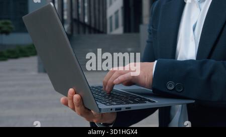 Nahaufnahme männlicher Hände, die Laptop in der Stadt schreiben nicht erkennbarer Geschäftsmann, der drahtlose Computergeräte in der Innenstadt unbekannter Geschäftsmann hält Stockfoto