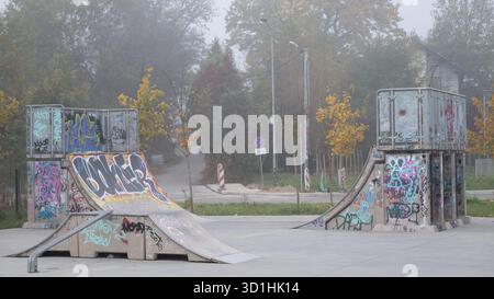 Krakau, Polen, Oktober 2025. Skatepark Strukturen bedeckt mit farbenfrohen Graffiti in einem Stadtpark an einem nebeligen Herbsttag. Öffentlicher Bereich für Skateboa Stockfoto