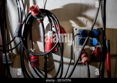 Industrielle Steckdosenleiste mit roten und blauen elektrischen Steckverbindern und Hochleistungs-Verlängerungskabeln, die das Stromverteilungssystem in der Werkstatt zeigen Stockfoto