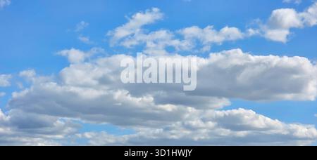 Weiche weiße Wolken ziehen über einen hellblauen Himmel, beleuchtet von sanftem Sonnenlicht, und schaffen eine ruhige und friedliche Atmosphäre. Stockfoto
