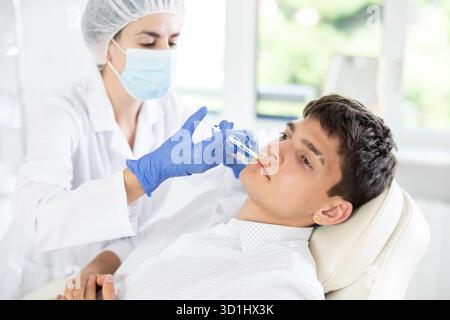 Professionelle Kosmetikerin Hände in Handschuhen, die eine Lippenverbesserung bei männlichen Klienten durchführen und Lippenfüller injizieren Stockfoto